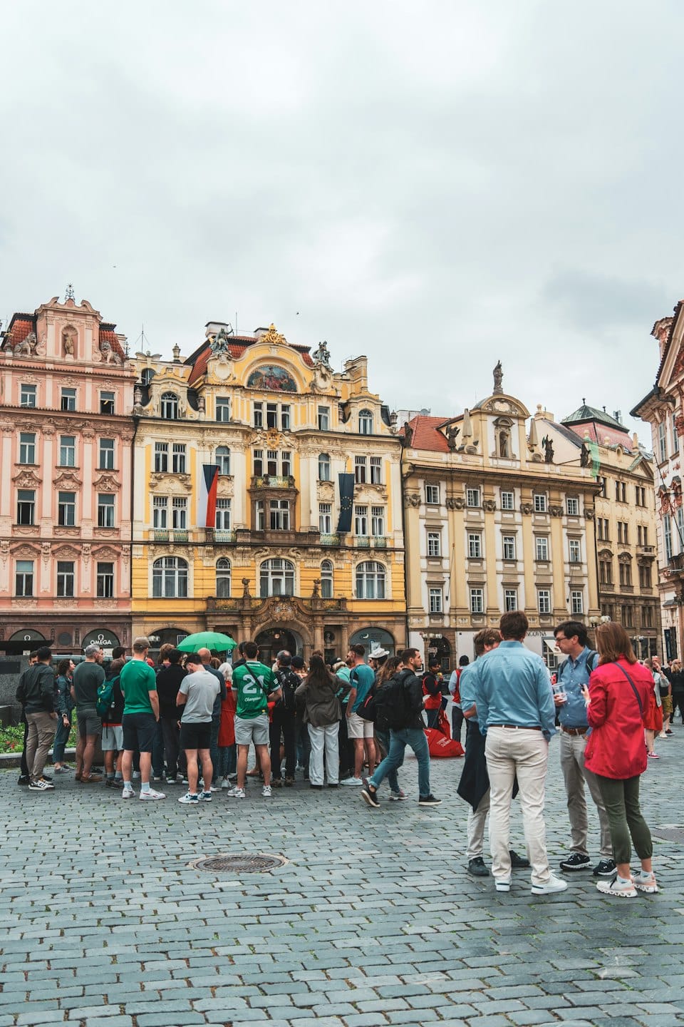 Skupina lidí si povídá na historickém dlážděném náměstí.